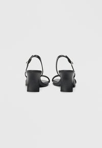 Black heeled sandals with a block heel, single strap design, and ankle buckle. Smooth leather texture and minimalistic style.