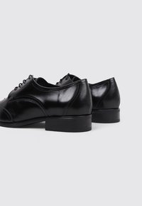 Zapatos de cuero negro con un acabado suave, punta redonda, diseño de cordones y un tacón bajo. Presentan costuras sutiles y acentos mínimos.