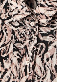 Camicia button-up con una base nera e motivi astratti a spirale di un rosa chiaro e bianco; tessuto in cotone dalla consistenza morbida.