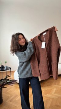 Brauner, flauschiger Cardigan mit langen Ärmeln, V-Ausschnitt und zwei Vorderaschen. Weßes Etikett ohne sichtbaren Text angebracht. Weiche Textur.