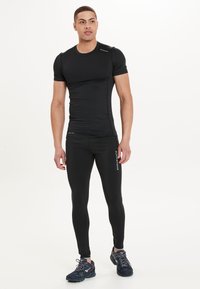 Svart träningsset bestående av en åtsittande kortärmad topp och matchande leggings, tillverkade av mjukt, elastiskt material med logotypdetaljer.