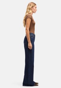 Granatowe dzwony z wysokim stanem, o gładkiej fakturze dżinsu i tradycyjnych kieszeniach, noszone z dopasowanym brązowym topem.