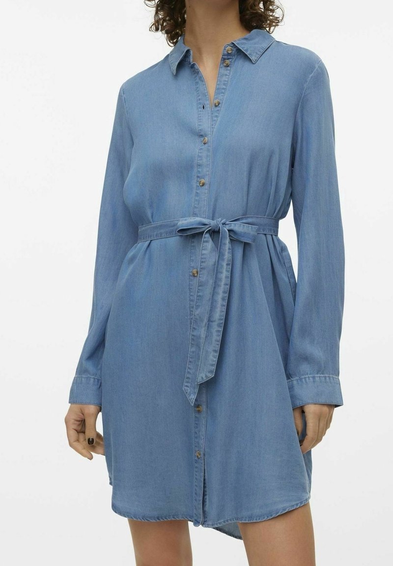 Abito camicia in denim di colore azzurro chiaro, presenta un colletto, maniche lunghe, apertura frontale con bottoni e cintura in vita. Texture morbida con una vestibilità comoda.