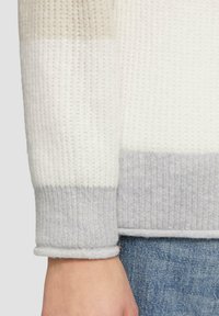 Gebreide trui met verticale ribbels in tinten wit en lichtgrijs en een omgeslagen zoom. De stof heeft een zachte, gestructureerde uitstraling.