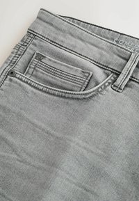 Szürke farmeranyag enyhén struktúrált felülettel. Elöl gombbal záródó zseb, és a varrások mentén kontrasztos varrás található.