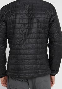 Svart isolerad jacka med ett quiltat mönster, utrustad med hög krage, långa ärmar och lätt konstruktion. Texturerad yta tydlig.