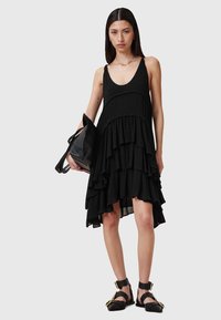 Vestido negro sin mangas con escote redondeado, dobladillo con volantes y tejido fluido. Combinado con un bolso negro y sandalias.