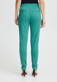 Tyrkysové nohavice so slim fit, s vertikálnymi čiernymi pruhmi. Elastický pás, dve zadné vrecká a upravený silueta.