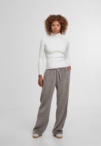 Biała żeberkowa sweter z golfem w połączeniu z luźnymi szarymi spodniami z kordurowej tkaniny, które mają elastyczny pas i sznurki.