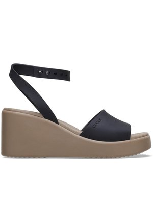 Zwarte open teen wedge sandal met een tan platformzool en een verstelbare enkelband met metalen studs voor bevestiging.