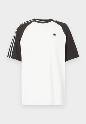 Bílé tričko s černými raglánovými rukávy, s modrými pruhovanými akcenty na ramenou a malým černým logem na hrudi.