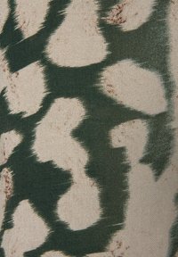 Stoff mit einem grünen und cremefarbenen abstrakten Muster, das Tierdrucke ähnelt, mit unregelmäßigen Formen und weicher Textur sowie subtilen Sprenkeln.