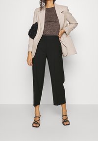 Beige kavaj över en brun strukturerad topp, parat med svarta cropped byxor och svarta sandaletter med remmar. Håller en svart strukturerad handväska.