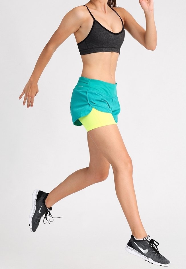 Conjunto deportivo que incluye un sujetador deportivo gris, pantalones cortos de correr turquesa con acentos amarillos y zapatillas de correr negras con una suela texturizada.