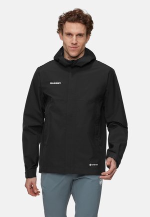 Veste imperméable noire avec capuche, dotée d'une fermeture éclair sur le devant, de poches latérales et des logos Mammut et Gore-Tex sur la poitrine et l'ourlet.