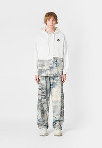 Sudadera blanca con un estampado gráfico en la parte inferior, combinada con pantalones sueltos de cuadro azul y gris. Zapatillas blancas de suela gruesa.