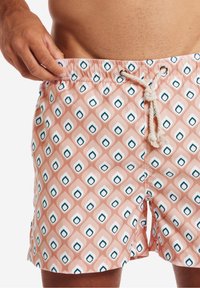 Simshorts i korall med ett geometriskt mönster av blå och vita diamanter. Har elastisk midja och justerbar dragsko.