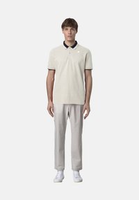 Polo beige con colletto e dettagli blu navy, abbinato a pantaloni grigi chiari e sneakers bianche. Tessuto liscio e stile semplice.