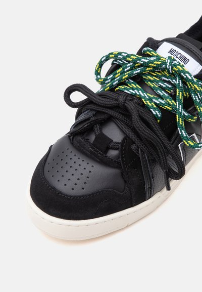 Μαύρο sneaker Moschino με διάτρητη μύτη, μαύρες λεπτομέρειες από σουέντ και δέρμα, και διπλά κορδόνια σε μαύρο και μοτίβο πράσινο-κίτρινο-άσπρο.