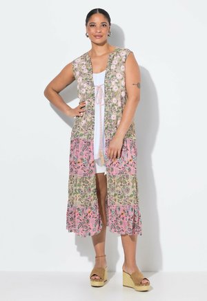 Gilet lungo a fantasia floreale con maniche corte, sezioni in rosa pastello e verde, apertura frontale e cravatta regolabile. Indossato sopra un vestito bianco.