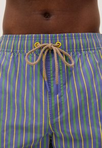 Costum de baie cu dungi în nuanțe de mov, verde și galben, cu talie ajustabilă prin șnur și capse galbene, realizat dintr-un material ușor și cu o textură netedă.
