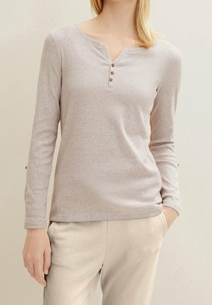 Lysebrun henley-skjorte med lange ærmer i tekstureret stof med tre knapper i brystet. Kombineret med lyse beige bukser uden synlige mønstre eller detaljer.