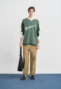 Zelen in bel pulover z na trakove, ohlapnega kroja, v kombinaciji s kavbojkami iz rjavega korduroja. Model drži črno torbo in nosi črne superge.