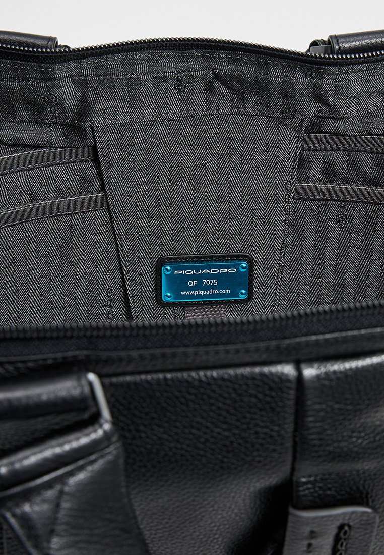 Wnętrze czarnej skórzanej torby z wzorem w jodełkę, wieloma przegródkami na karty oraz małą niebieską metką identyfikacyjną z nazwą marki.