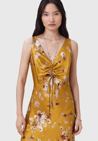 Abito in satin giallo con motivo floreale, scollatura a V, dettaglio arricciato sul davanti con lacci, senza maniche, texture liscia e lucentezza sottile.