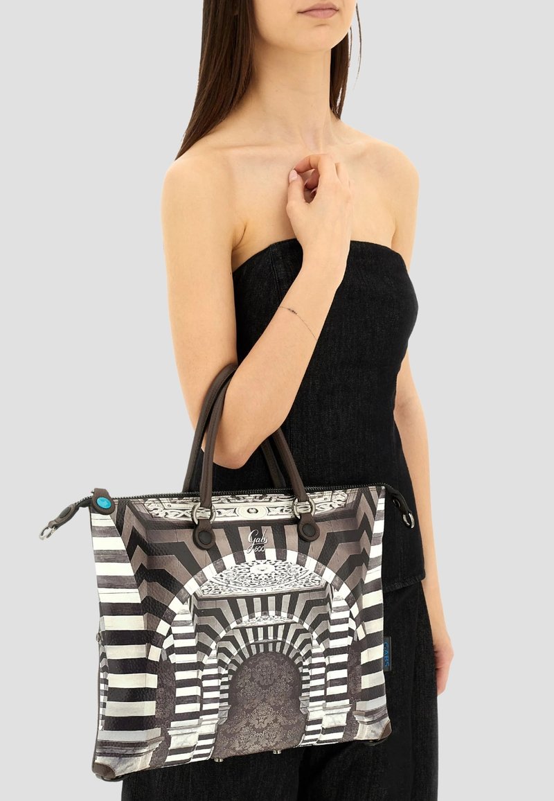 Donna che indossa un top senza spalline nero, mentre tiene una grande borsa con un motivo ad arco bianco e nero e manici marroni.