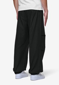 Svarta cargobyxor med avslappnad passform, utrustade med sidofickor och samlade muddar, parat med vita sneakers. Slät bomullstyg.