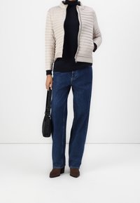 Lys beige quiltet jakke, marineblå turtleneck, blå brede jeans, brune hælede ankelstøvler og en sort skuldertaske med strop.