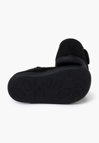 Zapato de ante negro con una suela de goma texturizada. Presenta un tacón plano y una puntera redondeada. La exhibición incluye detalles de fabricación visibles.