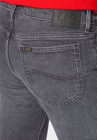 Dark grey jeans with a slim fit, featuring a black leather label at the waistband and golden stitching on the back pocket.