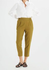 Olijfgroene broek met een elastische tailleband, tapered fit en zijzakken, gecombineerd met een wit overhemd met knopen en zwarte sandalen met bandjes.
