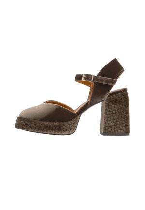Zapato de tacón alto de terciopelo marrón con tacón ancho, suela de plataforma texturizada y correa en el tobillo con una pequeña hebilla metálica.