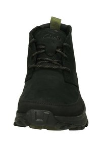 Botín negro de ante hasta el tobillo con puntera redonda, diseño de cordones, tirador de acento verde, suela rugosa y detalles texturizados en el talón.