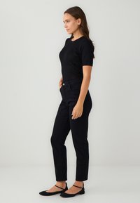 Czarny top z krótkim rękawem o subtelny połysku, w połączeniu z czarnymi spodniami w wąskim kroju. Stylizacja uzupełniona o czarne płaskie buty z paskami na kostkach.