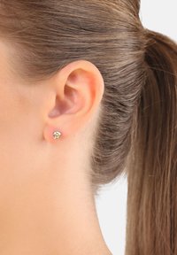 Pendiente de aro con strass claro, montado en un metal de tono plateado. Mostrado en la oreja de un modelo con el pelo liso recogido.