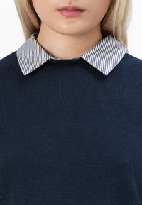 Pull en tricot bleu marine avec un col rond et un col rayé blanc et bleu. Texture lisse, détail du col visible.