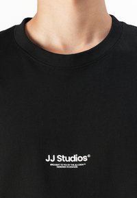 Sort bomulds T-shirt med rund hals, korte ærmer og hvide logodetaljer på brystet, med en glat tekstur.