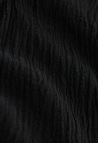 Must kangas kortsus tekstuuriga, millel on pehmed voldid ja õrn vertikaalne soonikmustriga.