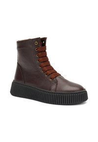 Botas de tobillo de cuero marrón con una suela de goma negra texturizada, ojales metálicos y cordones de tela marrones. Presenta una punta redonda y un cuello acolchado.