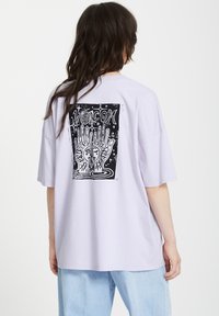 Lavendel oversized t-shirt met een zwarte grafische print op de achterkant met handen en gezichten, korte mouwen en een ontspannen pasvorm.