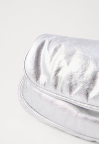 Borsa a pochette metallica argento con una superficie liscia e lucida, forma arrotondata e dettagli di pieghe sottili lungo la superficie e i bordi.