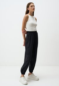 Top bianco senza maniche abbinato a pantaloni neri larghi e svasati con una cintura elastica e una leggera texture, completato da sneakers bianche.