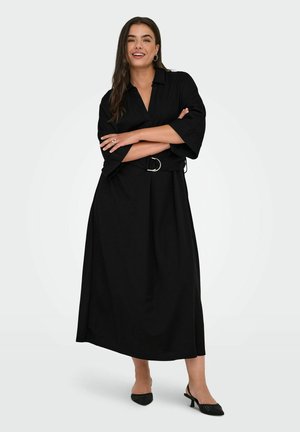 Vestido negro de largo hasta la rodilla, hecho de una tela suave, con cuello tipo camisa, mangas anchas y una cintura ceñida con un cinturón de hebilla plateada.