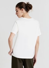 T-shirt en coton blanc à manches courtes, coupe droite et col rond. Le dos est uni, sans logos ni motifs visibles.