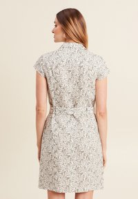 Abito marrone chiaro con motivo fogliare bianco, maniche corte, colletto e vita cinched. La vista posteriore mostra una trama liscia e un orlo a lunghezza ginocchio.