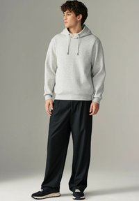 Sudadera de punto gris claro con un patrón texturizado, cordón y puños acanalados, combinada con pantalones negros holgados y zapatillas negras.